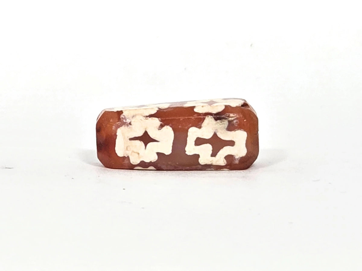 Fourth face of ancient carnelian eight-cross dzi bead showing paired floriate cross forms, natural carnelian colour variation from orange to deep reddish-brown, 22.9 mm × 9.4 mm