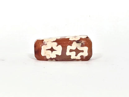 Fourth face of ancient carnelian eight-cross dzi bead showing paired floriate cross forms, natural carnelian colour variation from orange to deep reddish-brown, 22.9 mm × 9.4 mm