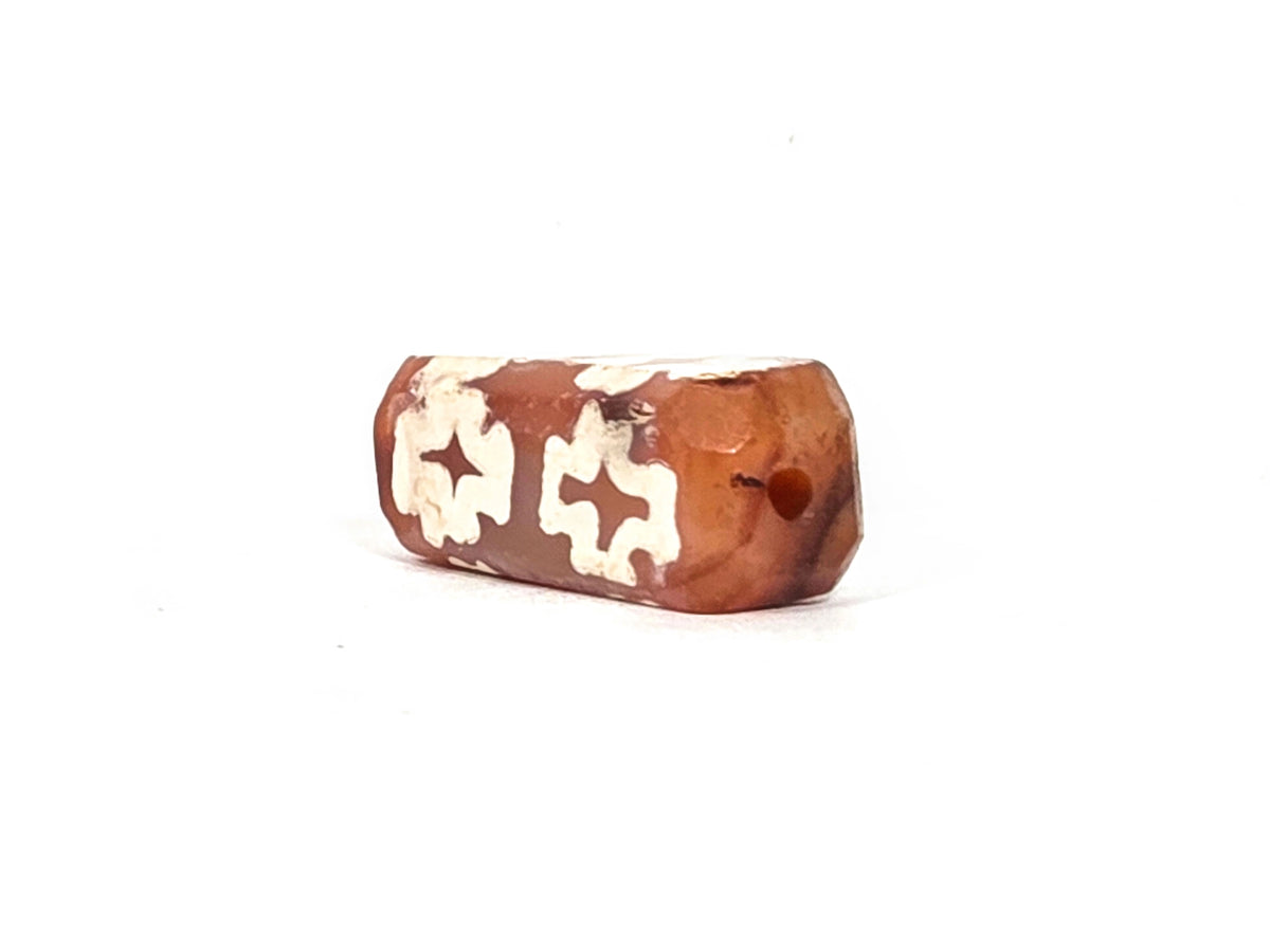 Angled end view of ancient etched carnelian dzi bead (AC-100126-CM8) showing small drill hole, beveled four-sided form, and warm translucent orange carnelian end face, 500–1000 years old