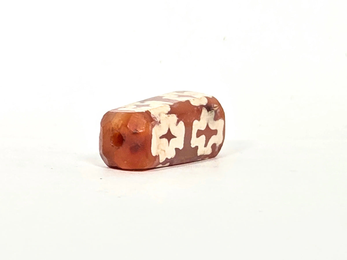 Second angled end view of ancient carnelian eight-cross dzi bead showing opposite drill hole, faceted beveled edges, and cream-white etching continuing to the end face