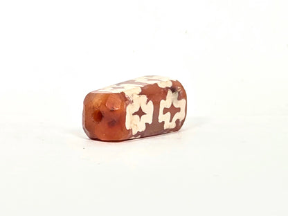 Second angled end view of ancient carnelian eight-cross dzi bead showing opposite drill hole, faceted beveled edges, and cream-white etching continuing to the end face