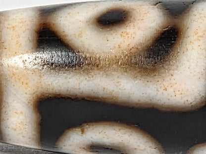 Macro surface detail of ancient nine-eye bloodspot dzi bead showing aged cream ridges, reddish-brown bloodspot mineral coloring, and centuries-old agate surface texture