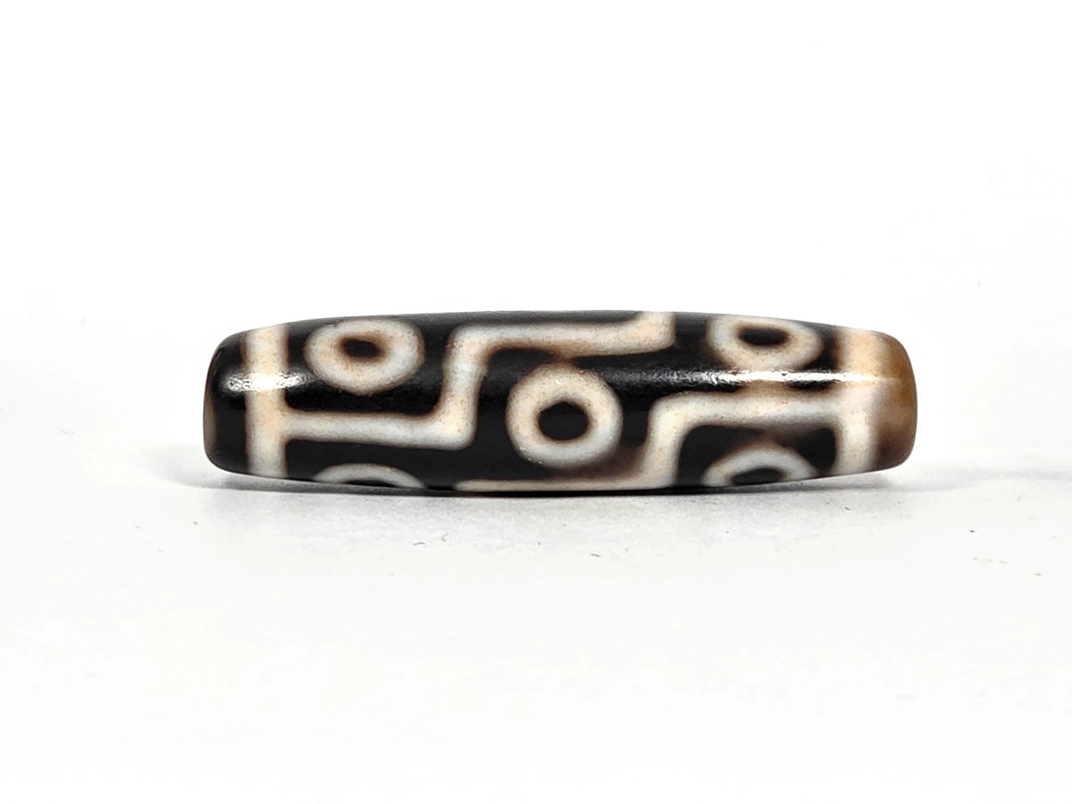 Ancient Tibetan nine-eye dzi bead AC-B-092526-9E, first lateral profile showing all nine eyes and cream-white maze-line pattern on deep black and brown agate, 500–800 years old