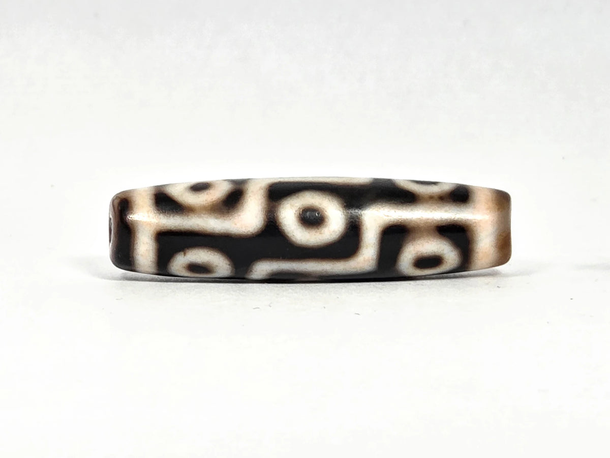 Third lateral profile of ancient Tibetan nine-eye dzi bead showing warm honey-brown edges and cream-white eye rings against black ground, 45.5 mm × 11.8 mm