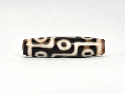 Third lateral profile of ancient Tibetan nine-eye dzi bead showing warm honey-brown edges and cream-white eye rings against black ground, 45.5 mm × 11.8 mm