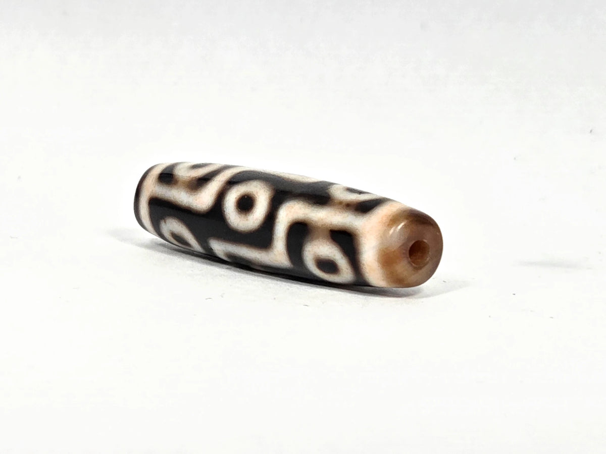 Angled end view of ancient nine-eye dzi bead AC-B-092526-9E showing original hand-drilled hole set in warm honey-brown agate end cap, 500–800 years old