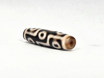 Angled end view of ancient nine-eye dzi bead AC-B-092526-9E showing original hand-drilled hole set in warm honey-brown agate end cap, 500–800 years old