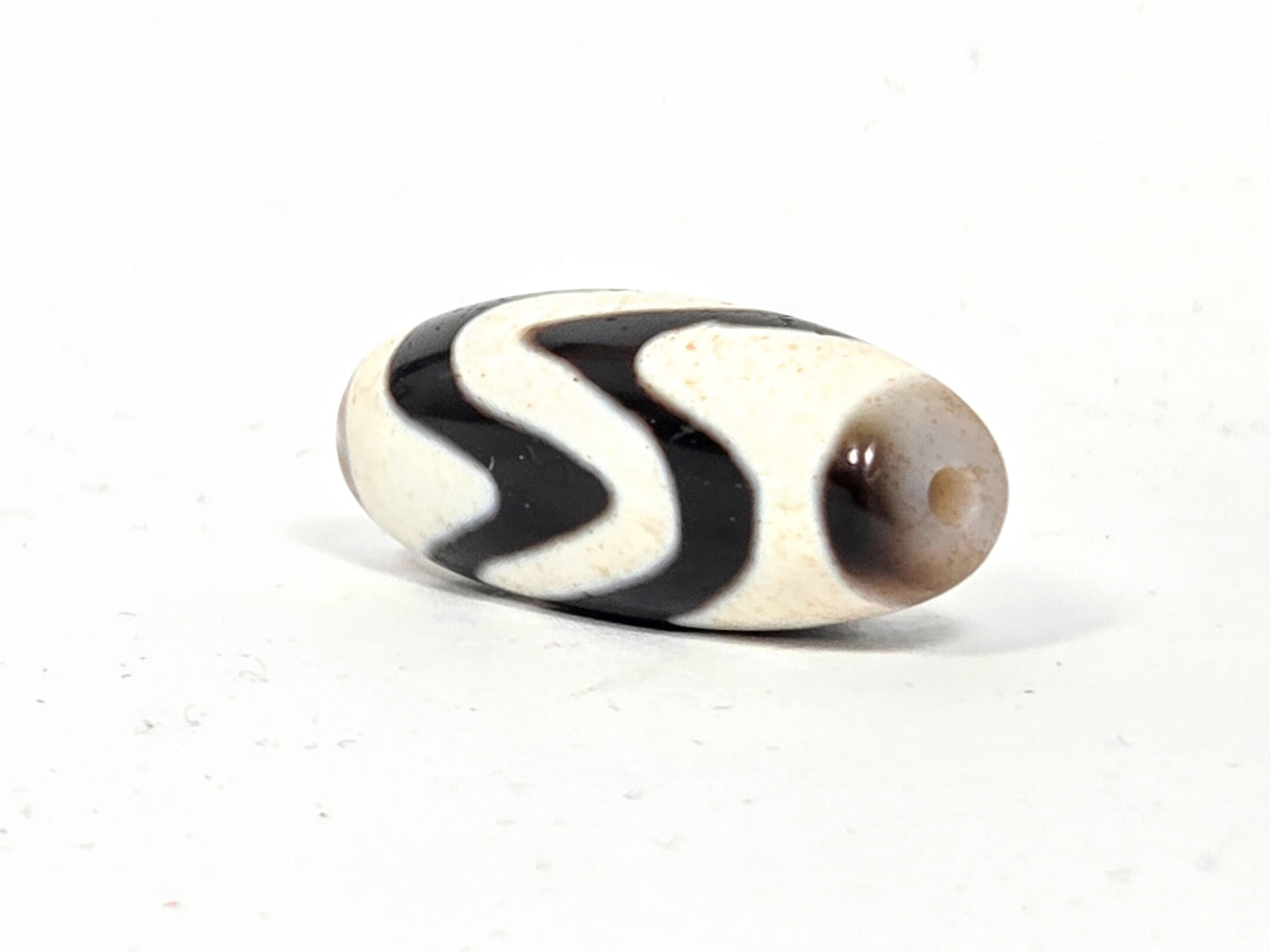 Ancient Tibetan Double Wave Dzi bead, angled view of second drill hole end — authentic age patina and natural agate surface — unretouched photo — Ancient Dzi Shop