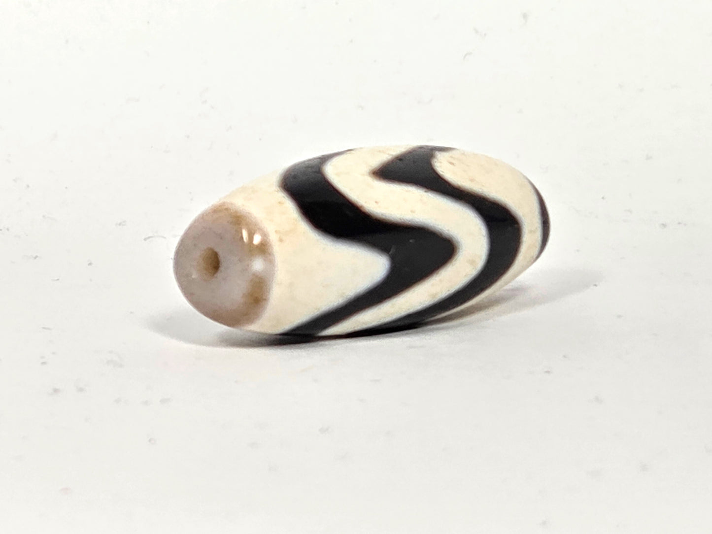 Angled view of ancient Tibetan Double Wave Dzi bead showing natural drill hole and agate body — 35.4mm × 14.0mm — unretouched photo — Ancient Dzi Shop