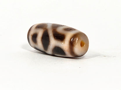 At-080926-6ELCBS antique Six Eye Lotus Cross dzi bead 24.1×10.8mm, angled drill-end view showing warm honey agate end cap and dark motif stripe elements, unretouched