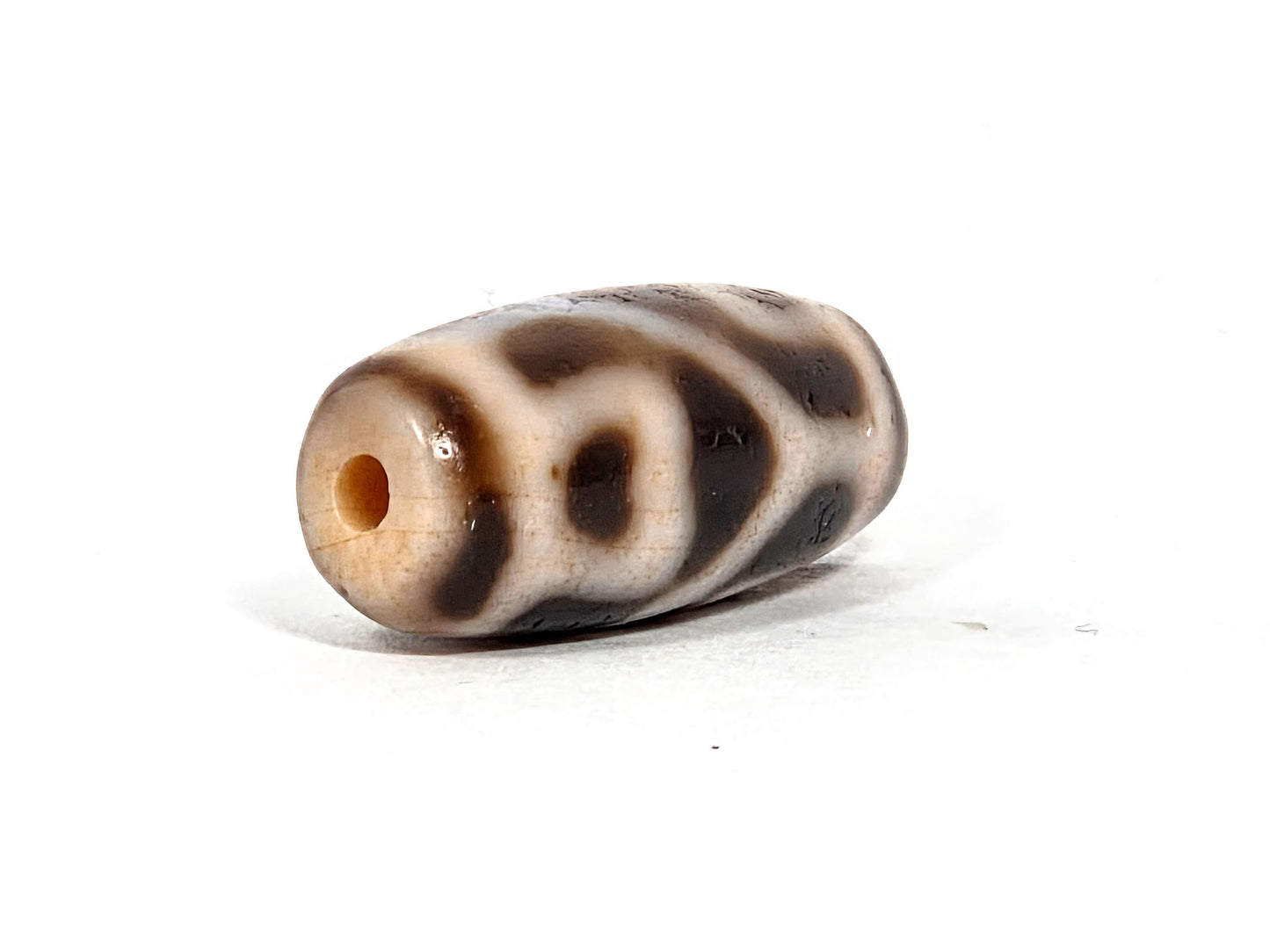 At-080926-6ELCBS antique Six Eye Lotus Cross dzi bead 24.1×10.8mm, opposite angled drill-end view showing cream end cap, drill hole, and oval eye forms, unretouched