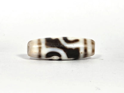 Second lateral profile of antique Tibetan twin lotus treasure vase dzi bead showing reverse face motif composition and cream-white ground with warm brown bloodspot speckling, 32.6 mm × 12.4 mm