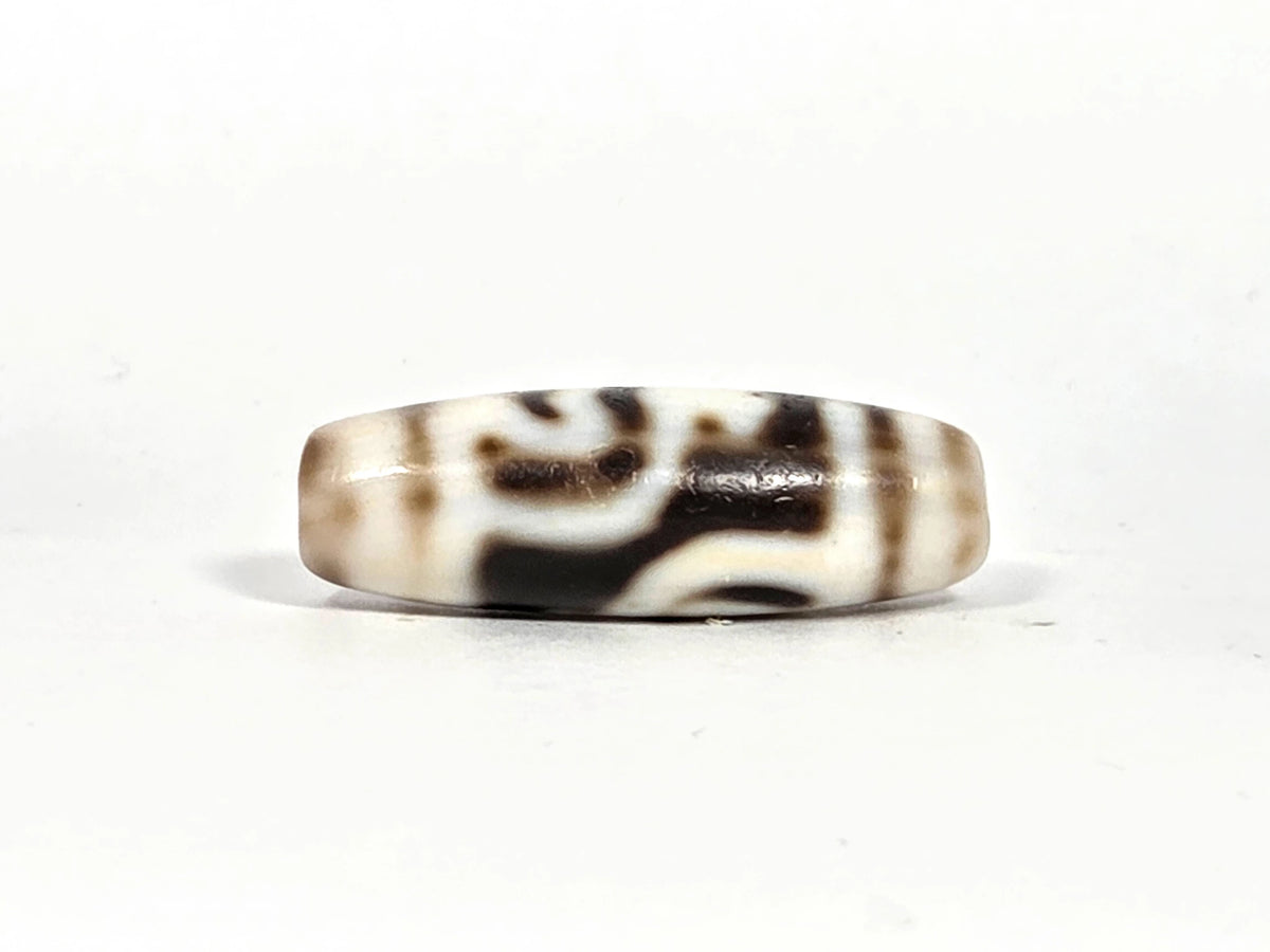 Fourth lateral profile of antique twin lotus treasure vase dzi bead showing complete motif composition on cream-white ground, horizontal band lines at equator, and dark brown-black marking pattern