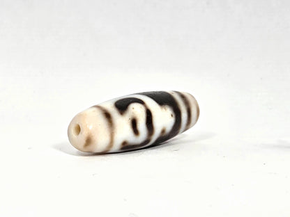 Opposite angled view of antique twin lotus treasure vase dzi bead showing second drill hole in cream-white tip, dark horizontal band pattern, and full barrel profile on cream agate ground
