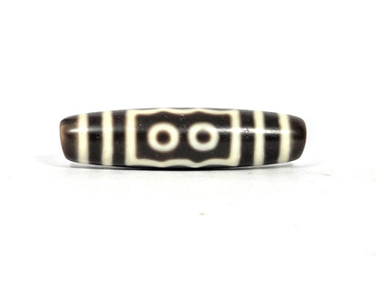 Two-eye face of antique five-eye dzi bead (AT-100826-5E) showing two cream-white eye rings within a rectangular cream border with wavy top and bottom edges on dark brown agate