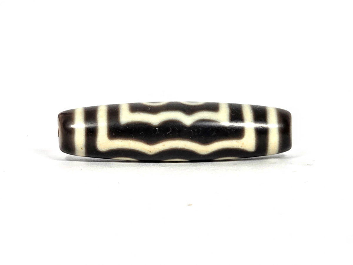 Second wave face of antique Tibetan five-eye dzi bead showing three undulating cream-white wave lines creating two dark channels on deep brown agate ground, 49.4 mm × 12.7 mm