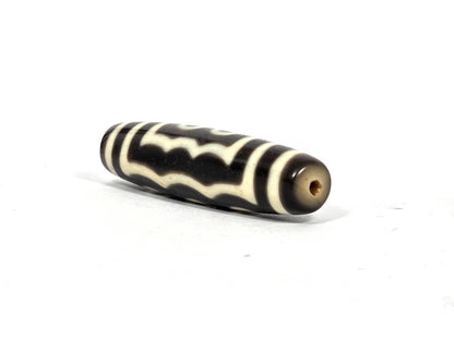 Angled end view of antique Tibetan five-eye dzi bead (AT-100826-5E) showing small clean drill hole in warm grey-brown agate end cap, 200–400 years old