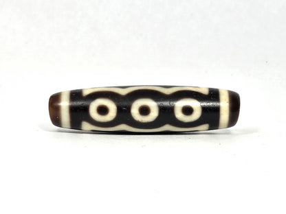 Antique Tibetan five-eye dzi bead (AT-100926-5E2), three-eye face showing three cream-white eye rings beneath a scalloped cloud-wave line on deep dark brown and black agate, 48.9 mm, 200–400 years old
