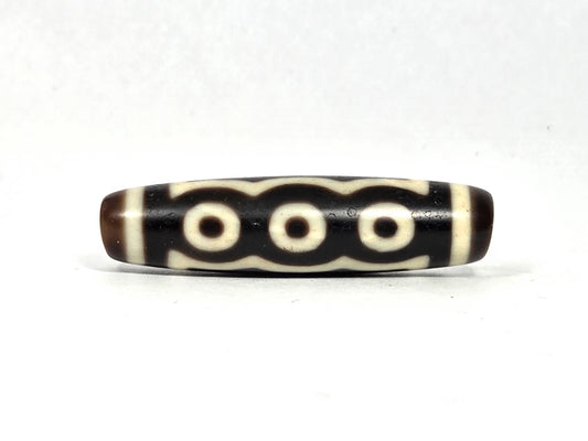 Antique Tibetan five-eye dzi bead (AT-100926-5E2), three-eye face showing three cream-white eye rings beneath a scalloped cloud-wave line on deep dark brown and black agate, 48.9 mm, 200–400 years old