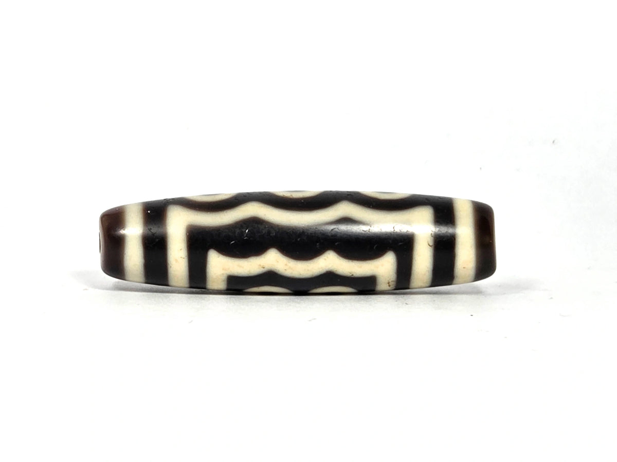Wave face of antique Tibetan five-eye dzi bead showing dense stacked scalloped wave layers in cream-white on dark brown-black agate ground with cream horizontal base band, 48.9 mm