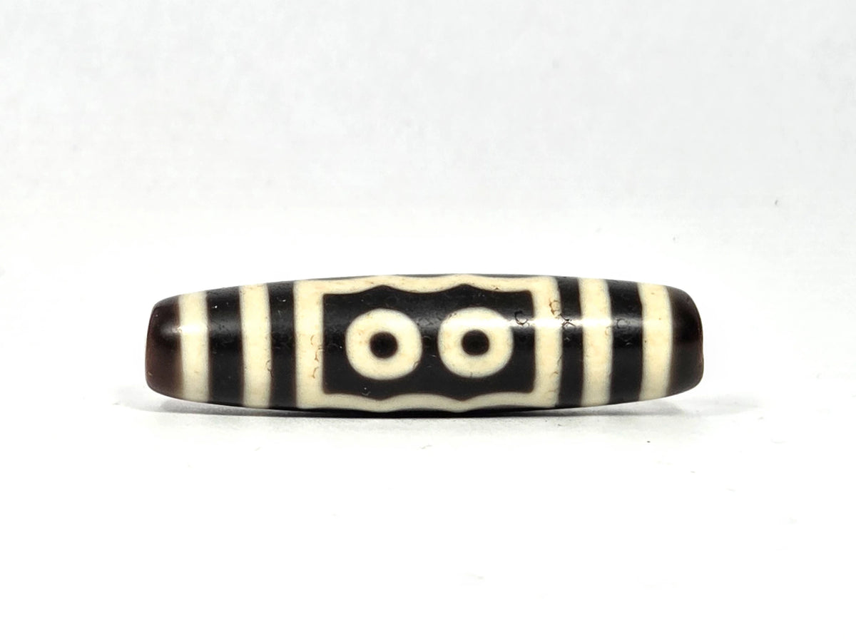 Two-eye face of antique five-eye dzi bead (AT-100926-5E2) showing two cream-white eye rings within a rectangular frame with scalloped top edge on dark brown-black agate ground