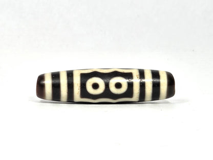 Two-eye face of antique five-eye dzi bead (AT-100926-5E2) showing two cream-white eye rings within a rectangular frame with scalloped top edge on dark brown-black agate ground