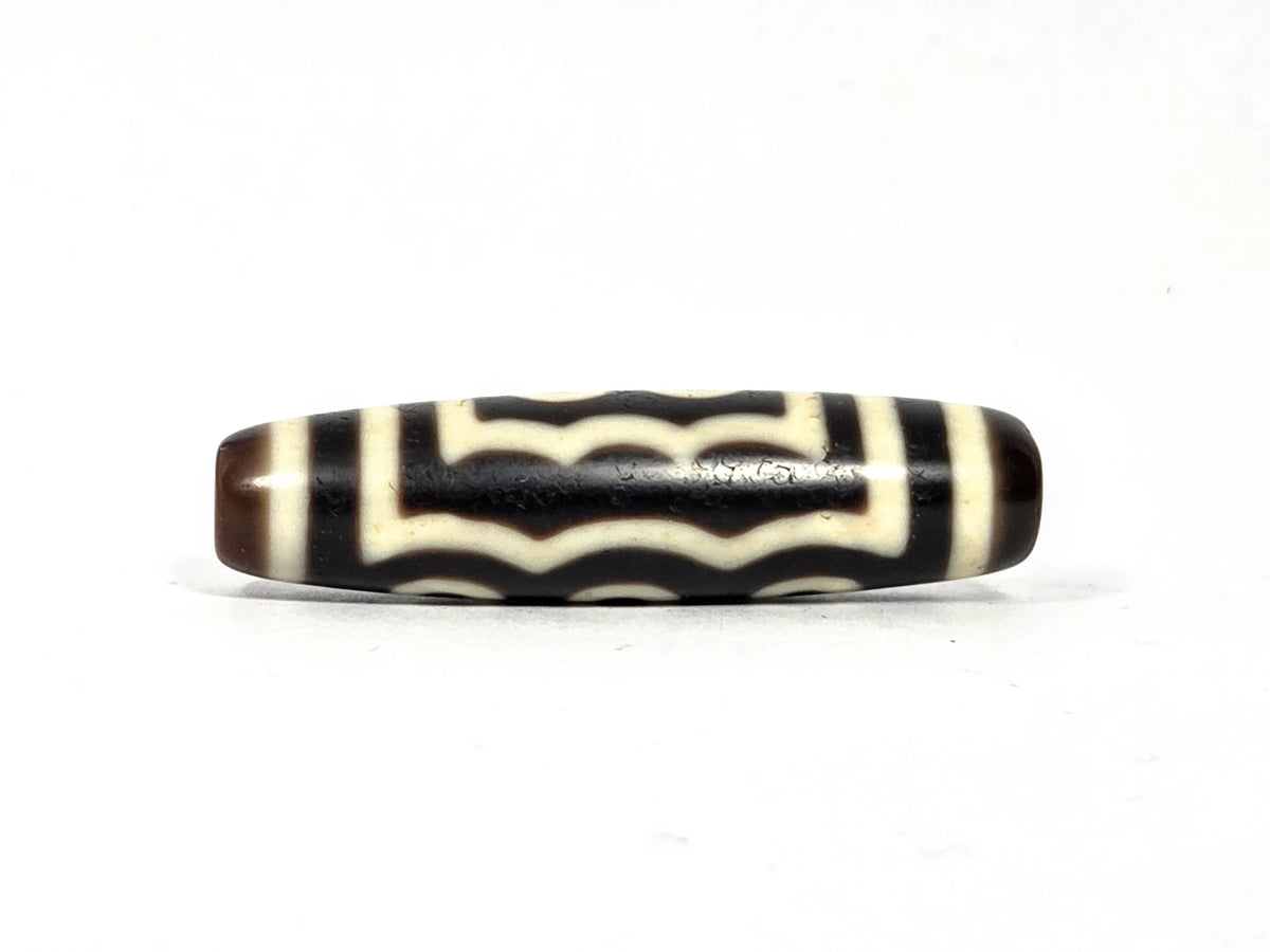 Second wave face of antique Tibetan five-eye dzi bead showing four to five stacked undulating cream-white wave lines on dark brown-black agate, 48.9 mm × 12.7 mm