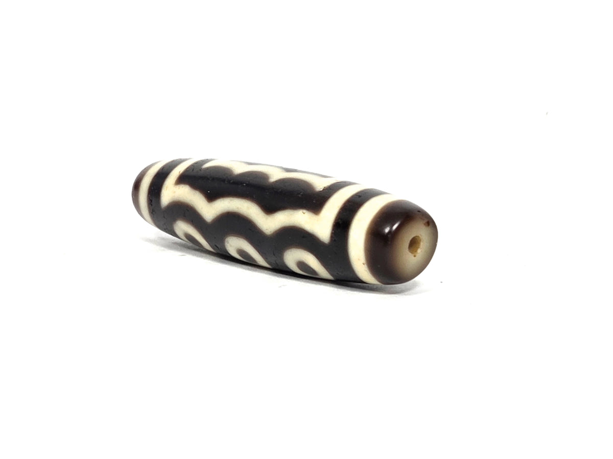 Angled end view of antique Tibetan five-eye dzi bead (AT-100926-5E2) showing small clean drill hole in warm brown agate end cap, elongated barrel form, 200–400 years old