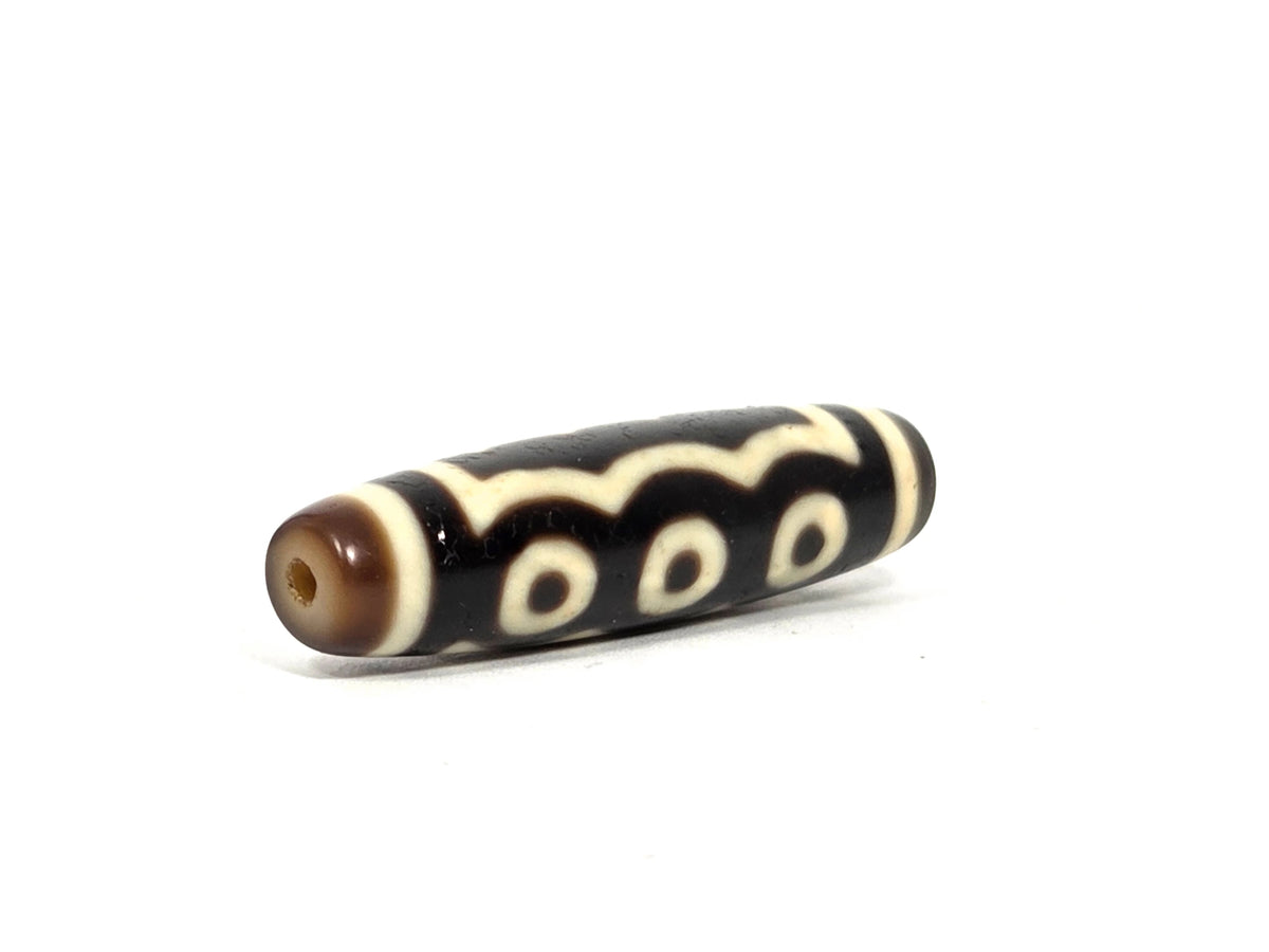 Opposite end view of antique Tibetan five-eye dzi bead showing second drill hole and warm brown end cap zone, scalloped wave pattern visible continuing to the tip