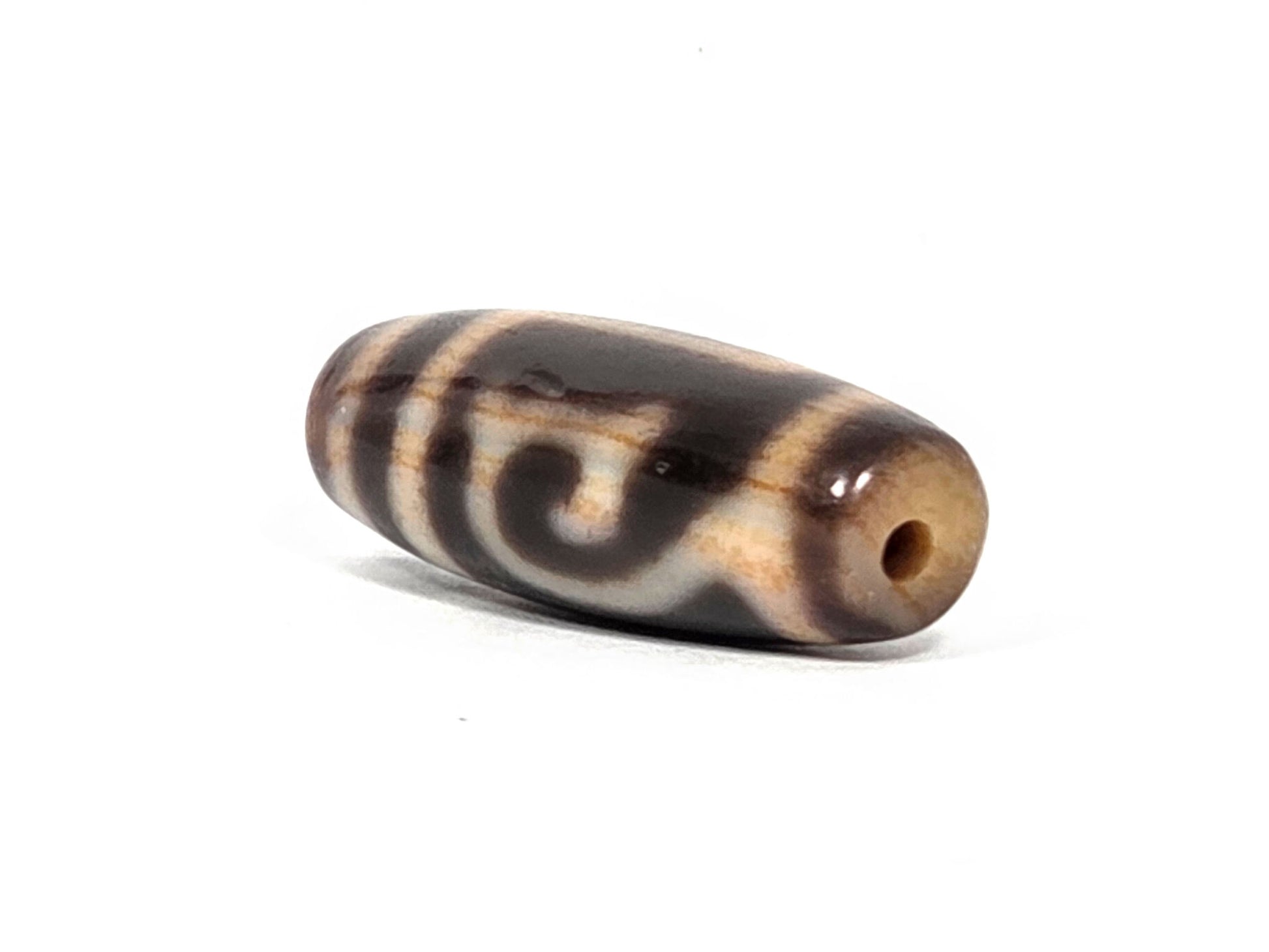 At-082326-GTBS antique Green Tara dzi bead 30.3×11.3mm, angled drill-end view showing medicine dig raised mark above drill hole and warm honey agate channel, unretouched