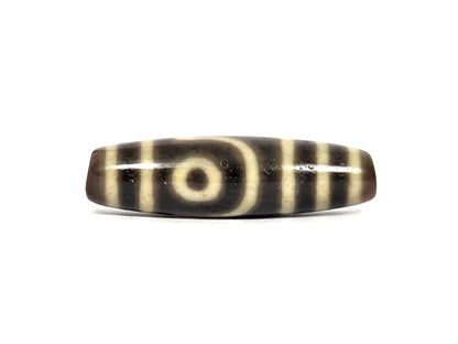 Antique Tibetan two eye dzi bead AT-102126-2E, first face — cream-white eye with dark pupil framed by a curved cream line, cream bands at both ends, on dark brown agate that photographs near-black, 200–400 years old
