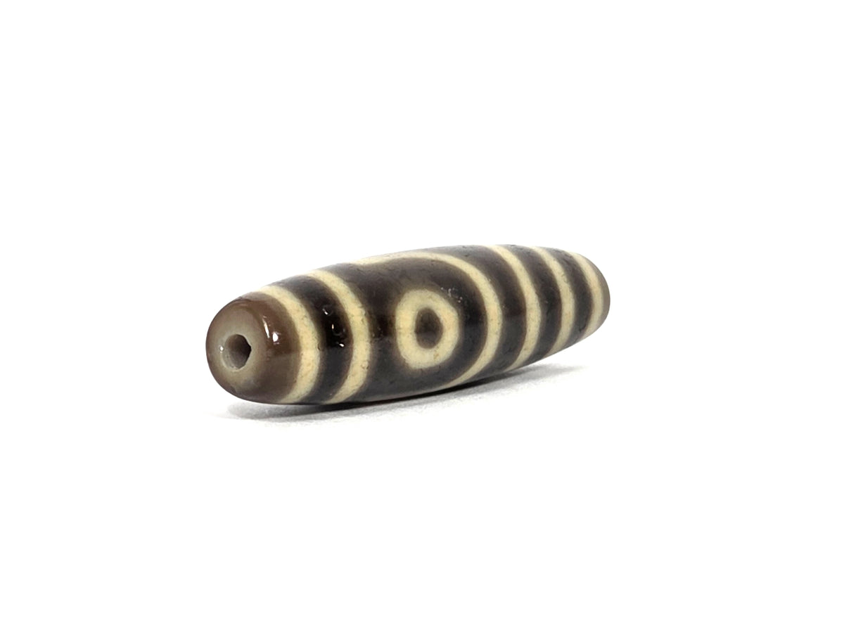 Opposite angled end view of antique Tibetan two eye dzi bead AT-102126-2E showing second drill hole in translucent brown agate tip, framed cream eye close to that end, and cream bands toward the far end, 200–400 years old