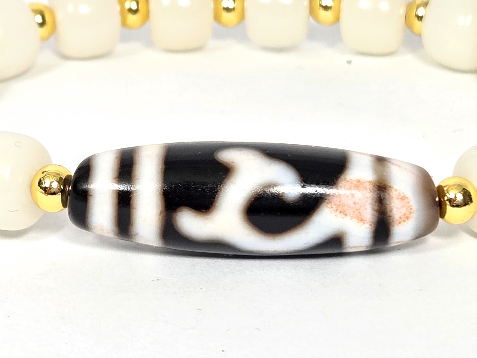 Close-up of antique Tibetan Green Tara Dzi focal bead in bracelet setting — Tara motif with natural bloodspots and rose-amber inclusions, flanked by gold-tone spacers and white bodhi root — unretouched photo — Ancient Dzi Shop