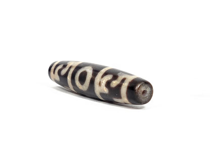 Angled end view of new Taiwan three-eye Guru Rinpoche paraphernalia dzi bead (N-092726-GRP3E) showing small clean drill hole set in deep brown-black agate tip, elongated torpedo form visible