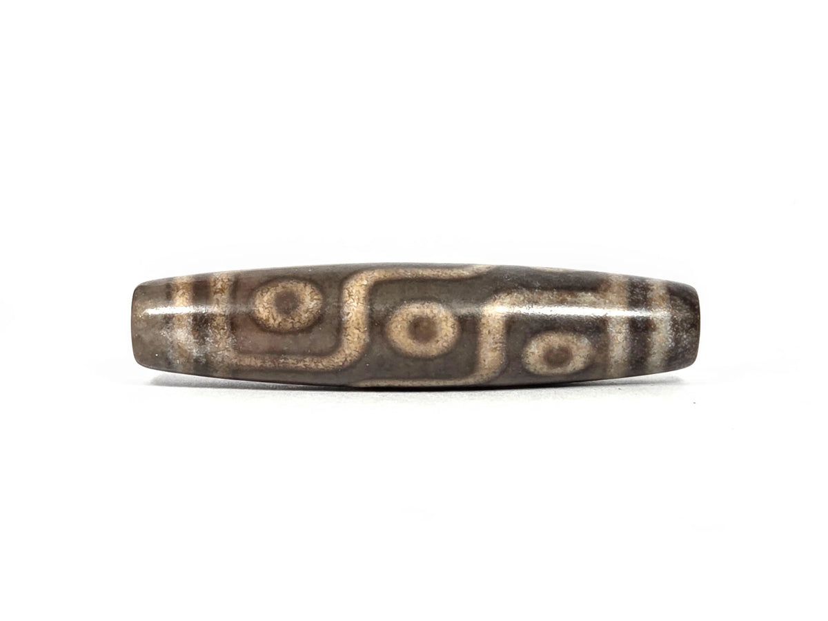 New nine-eye dzi bead N-101026-9E, first lateral profile showing all nine eyes with cream-tan rings and dark centers connected by S-curve maze-line network on deep charcoal-grey agate ground, 58.5 mm
