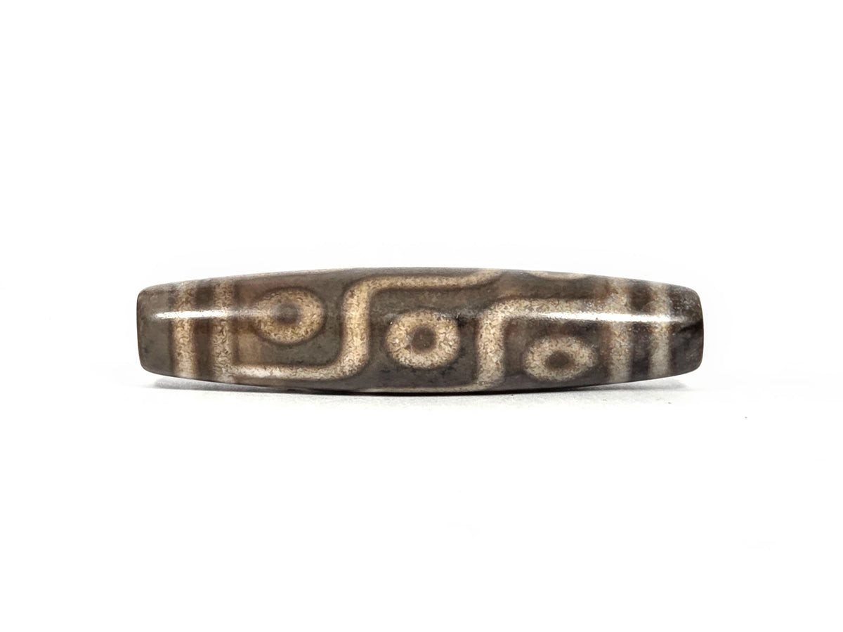 Second lateral profile of new nine-eye dzi bead showing reverse face eye pattern and warm cream-tan maze-line network on dark grey-brown agate, 58.5 mm × 13.1 mm