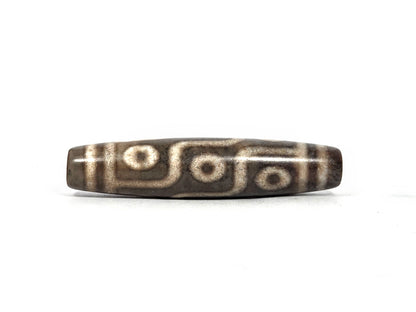 Third lateral profile of new nine-eye dzi bead N-101026-9E showing full elongated barrel form, end cap band lines, and complete nine-eye composition on deep charcoal-grey agate