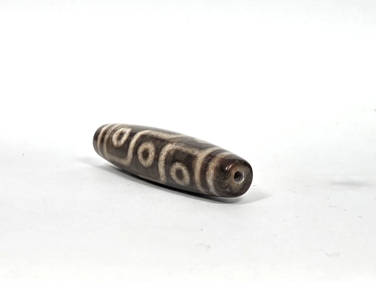 Opposite end view of new nine-eye dzi bead N-101026-9E showing second drill hole aperture and dark charcoal agate tip with cream-tan band line detail