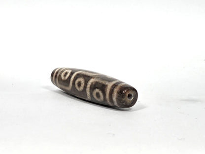 Opposite end view of new nine-eye dzi bead N-101026-9E showing second drill hole aperture and dark charcoal agate tip with cream-tan band line detail