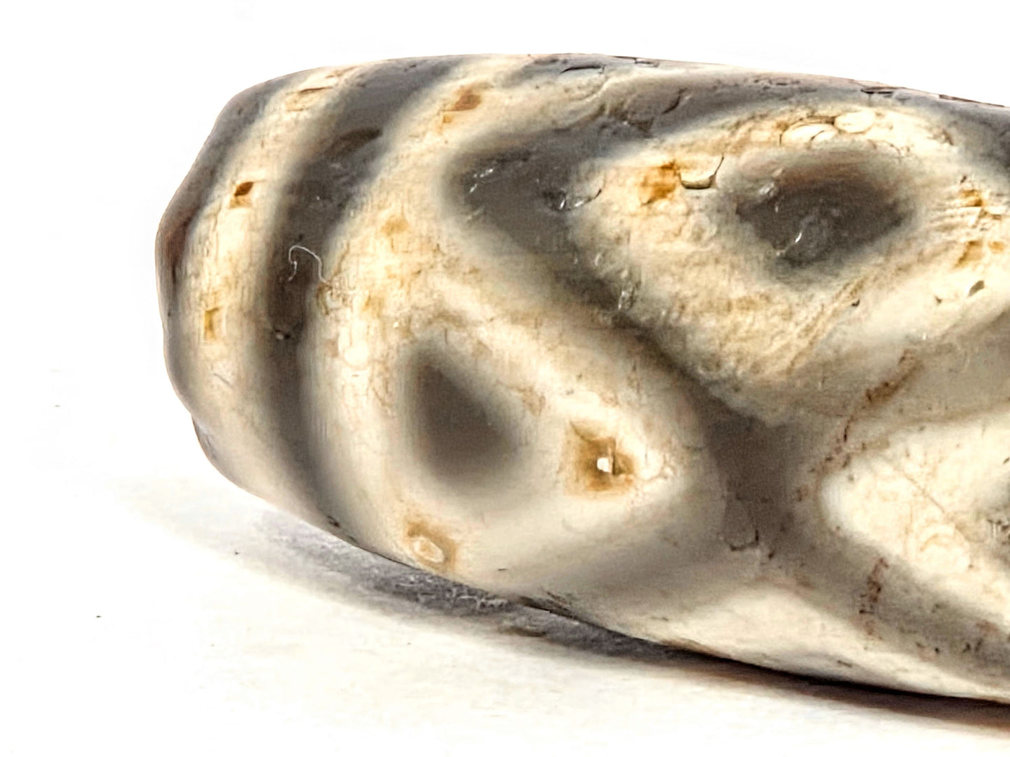 lose-up of Three Diamond Eye and Tiger Tooth motif on ancient Tibetan Dzi bead — bold dark etching on warm cream agate