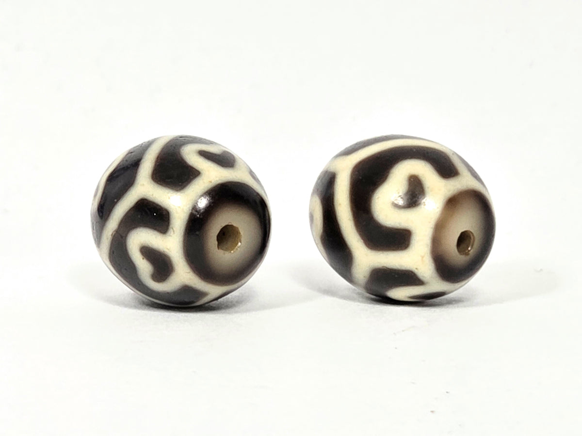 Drill hole end view of antique Tibetan Six Eye Lotus round Dzi bead pair showing swirl and lotus petal pattern surrounding natural agate drill holes — unretouched photo — Ancient Dzi Shop
