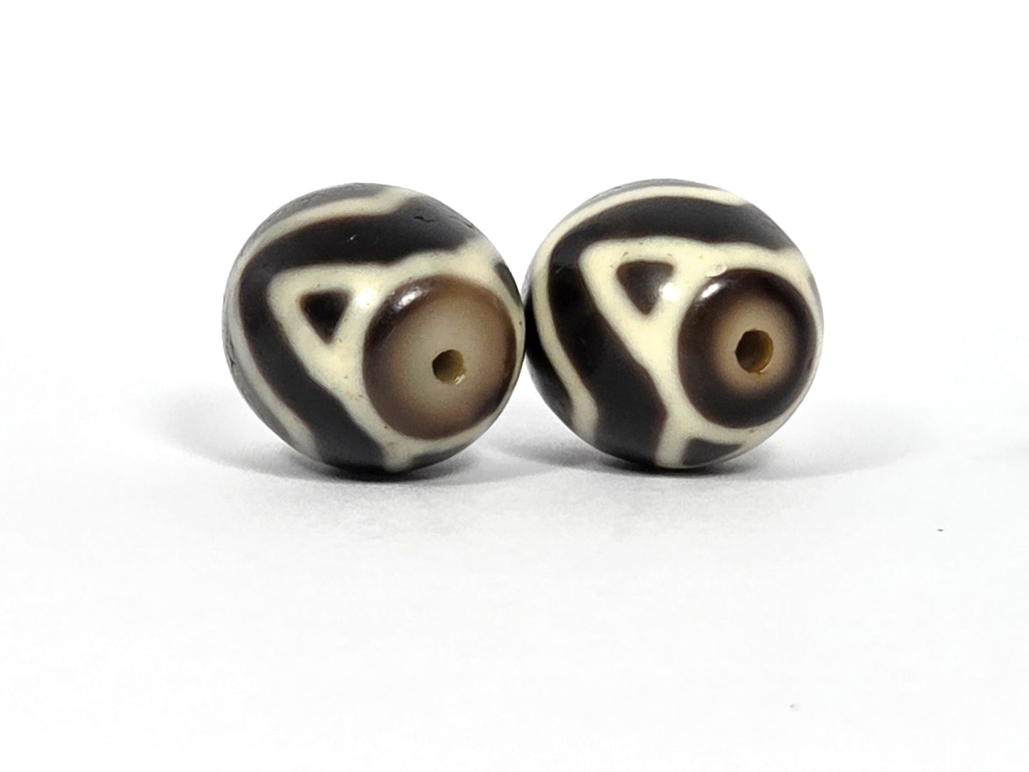 At-070626-TTW antique round Wave Tiger Tooth dzi pair, drill-end face view: Bead A cool grey-beige end cap, Bead B warm honey-brown end cap, unretouched