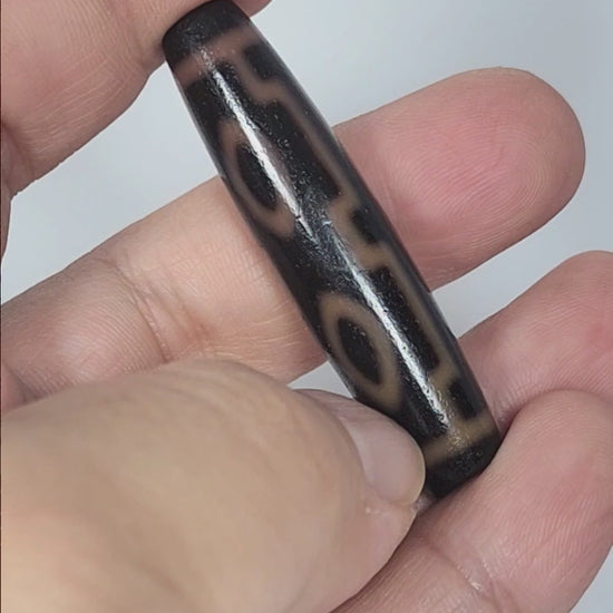 Video of antique Tibetan Four Eye dzi bead At-012325-4E rotating 360°, warm amber-orange eye rings on deep dark brown agate, full torpedo 51.9mm × 12.2mm, unretouched footage