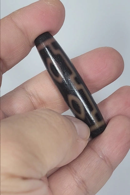 Video of antique Tibetan Four Eye dzi bead At-012325-4E rotating 360°, warm amber-orange eye rings on deep dark brown agate, full torpedo 51.9mm × 12.2mm, unretouched footage