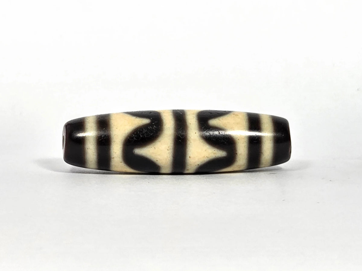 Third lateral profile of antique double wave dzi bead (AT-092826-DW2) showing full motif composition, deep black wave forms on cream-white ground, 40.4 mm × 11.4 mm