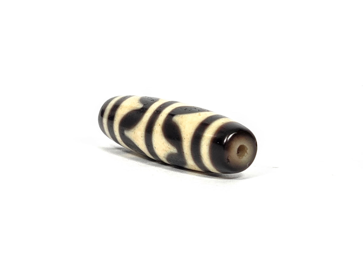 Angled end view of antique Tibetan double wave dzi bead showing small clean drill hole set in warm dark brown agate end cap, 200–400 years old