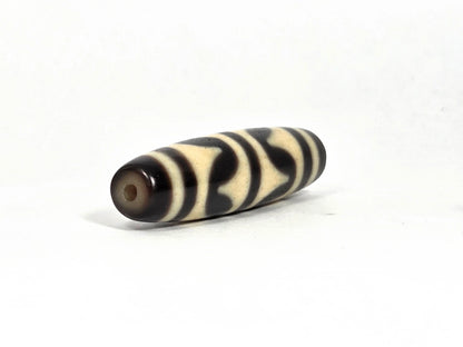 Opposite end view of antique Tibetan double wave dzi bead (AT-092826-DW2) showing second drill hole and warm brown end cap zone with black and cream wave pattern continuing to the tip