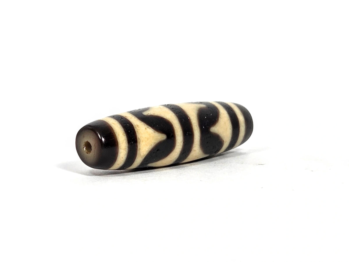 Opposite end view of antique Tibetan double wave dzi bead (AT-092826-DW) showing second drill hole and warm brown end cap zone with black and cream wave pattern continuing to the tip