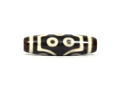 Second lateral profile of antique seven-eye dzi bead showing two eyes flanked by angular bracket forms and maze-line connectors on dark brown-black ground, cream-white motif, 39.7 mm