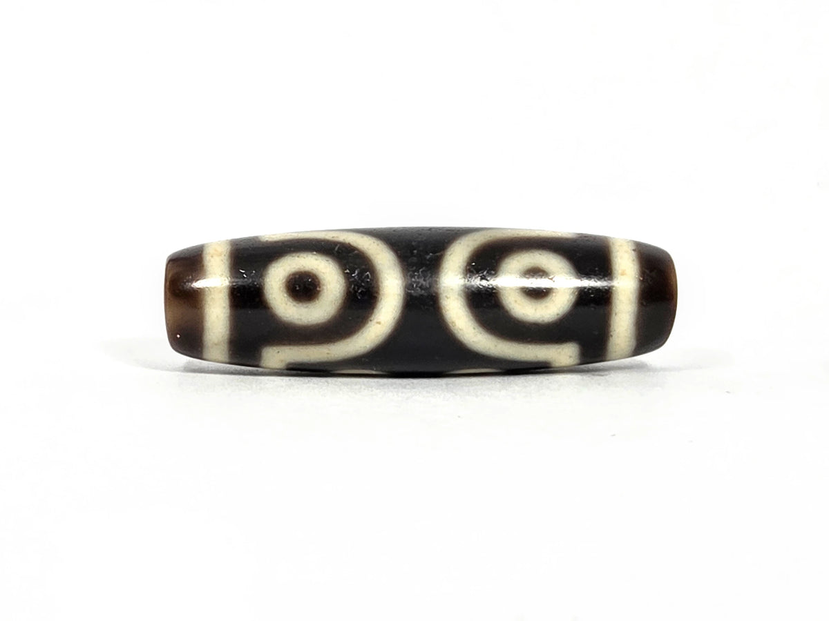 Third lateral profile of antique Tibetan seven-eye dzi bead showing two large eyes with scroll connectors and cream-white rings on deep brown-black agate ground, 39.7 mm × 11.7 mm